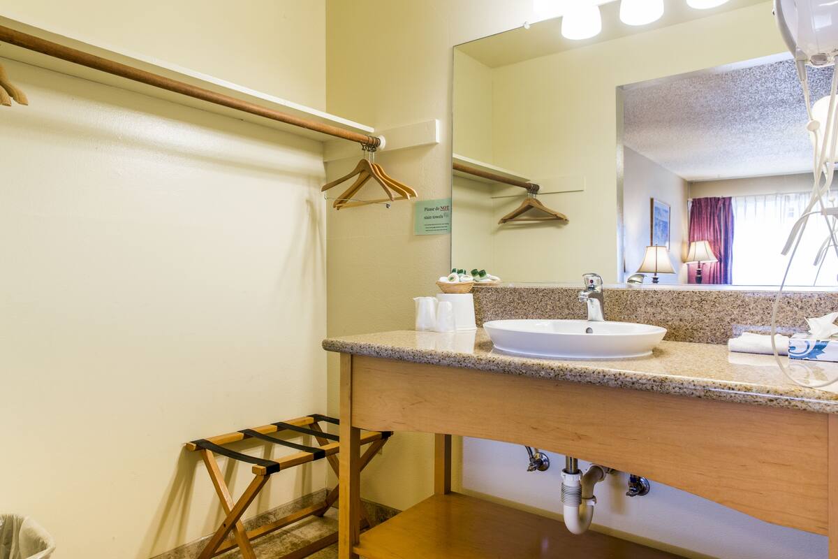 A hotel bathroom with a sink, mirror, towel rack, and a sign indicating the room type.