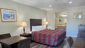 A hotel room with a bed, a desk, a chair, a nightstand with a lamp, a telephone, and a painting on the wall. - San Luis Inn And Suites (San Luis Obispo)
