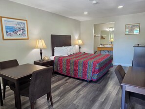 A hotel room with a bed, a desk, a chair, a nightstand with a lamp, a telephone, and a painting on the wall. - San Luis Inn And Suites (San Luis Obispo)