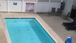 A rectangular swimming pool with a clear blue water, surrounded by a white fence, and a few lounge chairs. - San Luis Inn And Suites (San Luis Obispo)