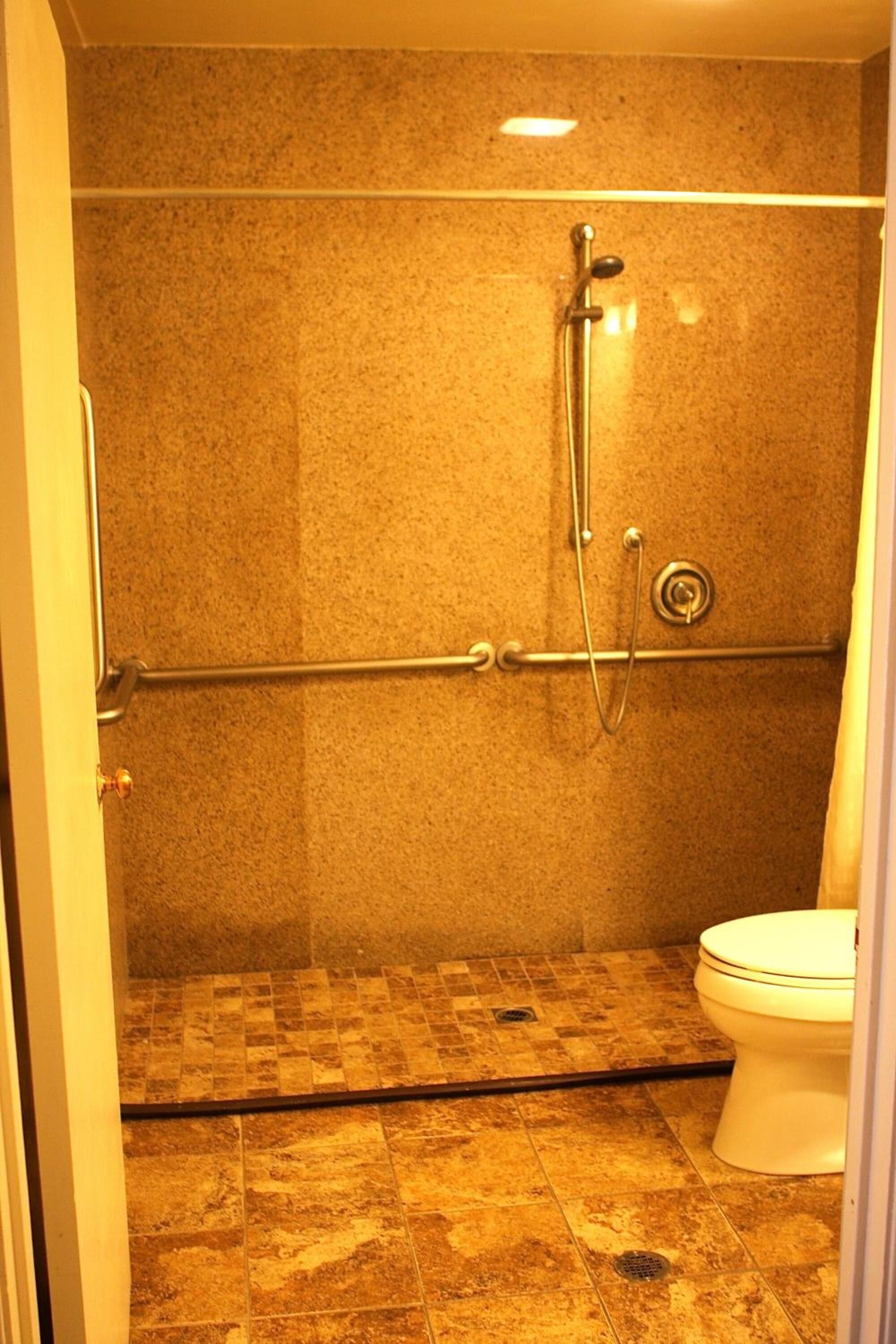 A bathroom with a shower, toilet, and tiled floor.