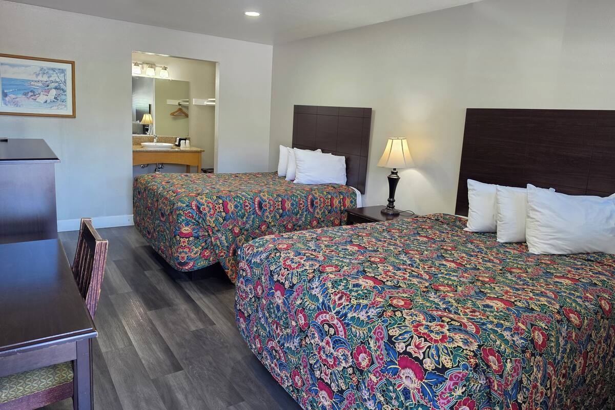 A hotel room with two beds, a desk, a chair, a mirror, and a lamp.