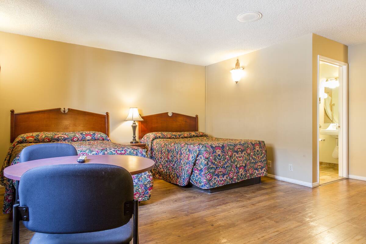 A hotel room with two beds, a small table, and a chair.
