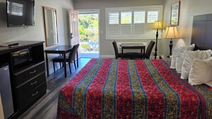 A hotel room with a bed, desk, chair, television, and a view of the outdoors. - San Luis Inn And Suites (San Luis Obispo)