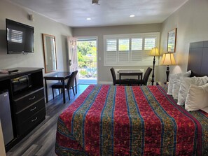 A hotel room with a bed, desk, chair, television, and a view of the outdoors. - San Luis Inn And Suites (San Luis Obispo)