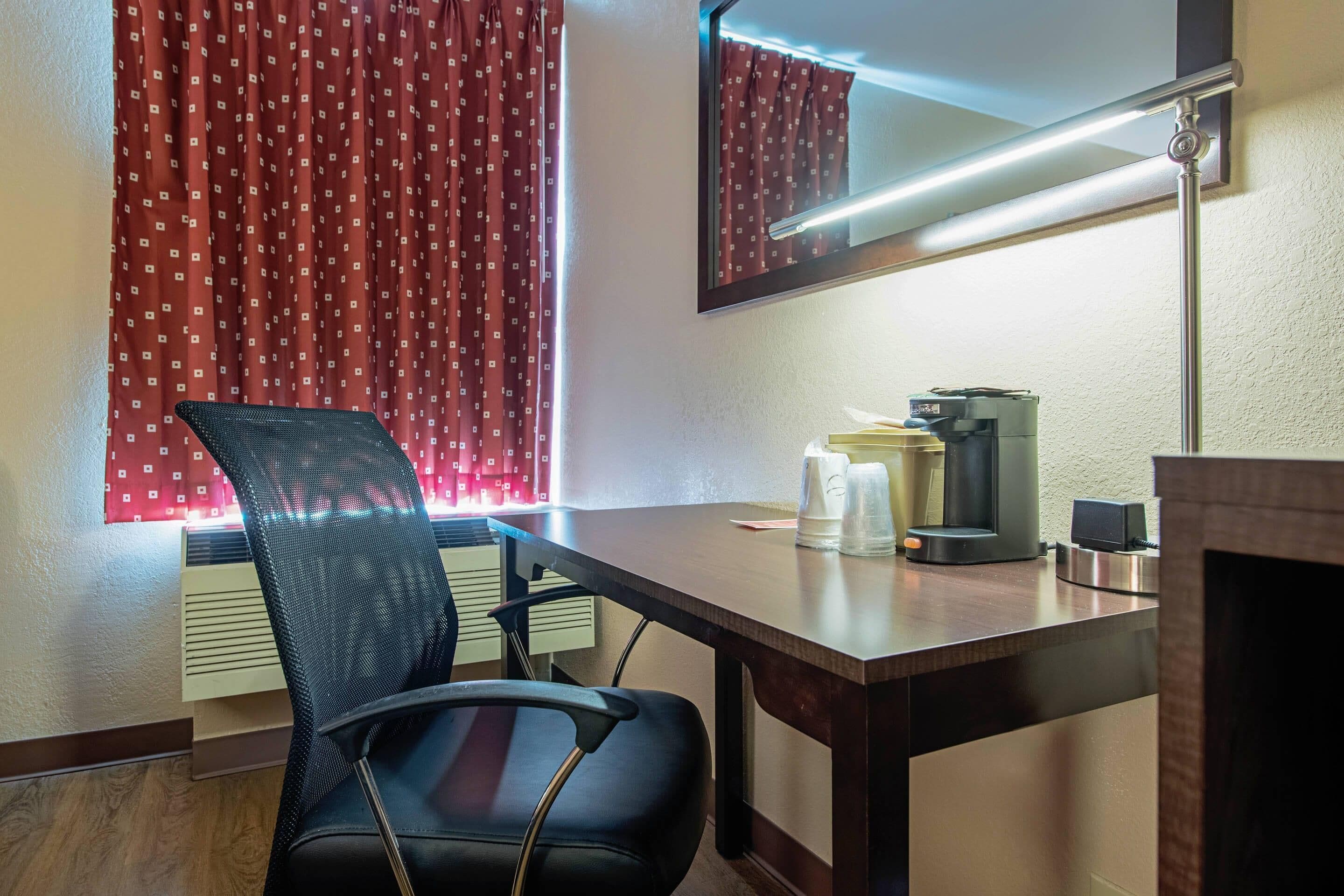 A hotel room with a desk, chair, coffee maker, and a mirror.