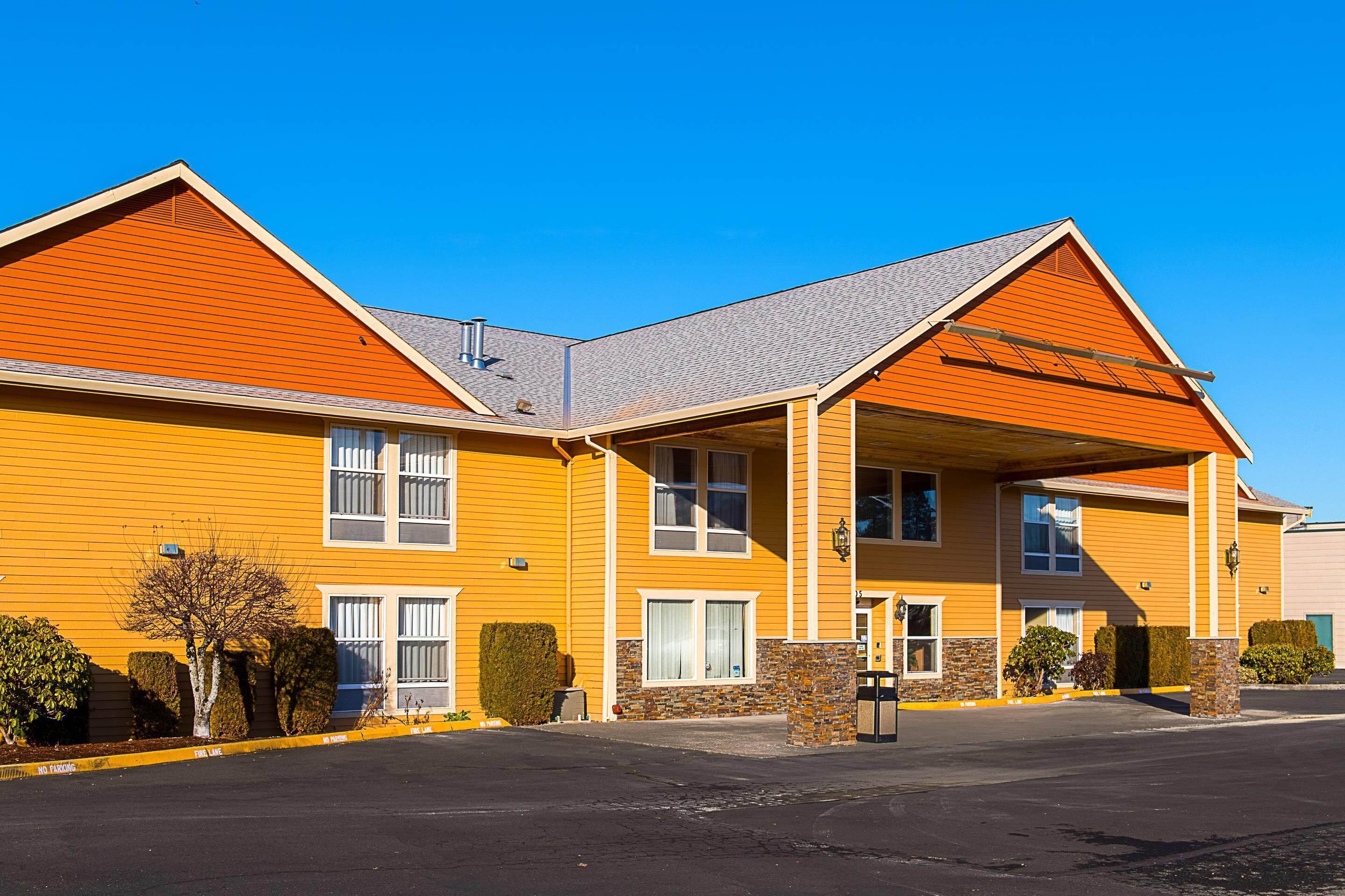 A two-story hotel with a yellow facade, a covered entrance, and a parking lot.