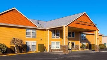 A two-story hotel with a yellow facade, a covered entrance, and a parking lot.