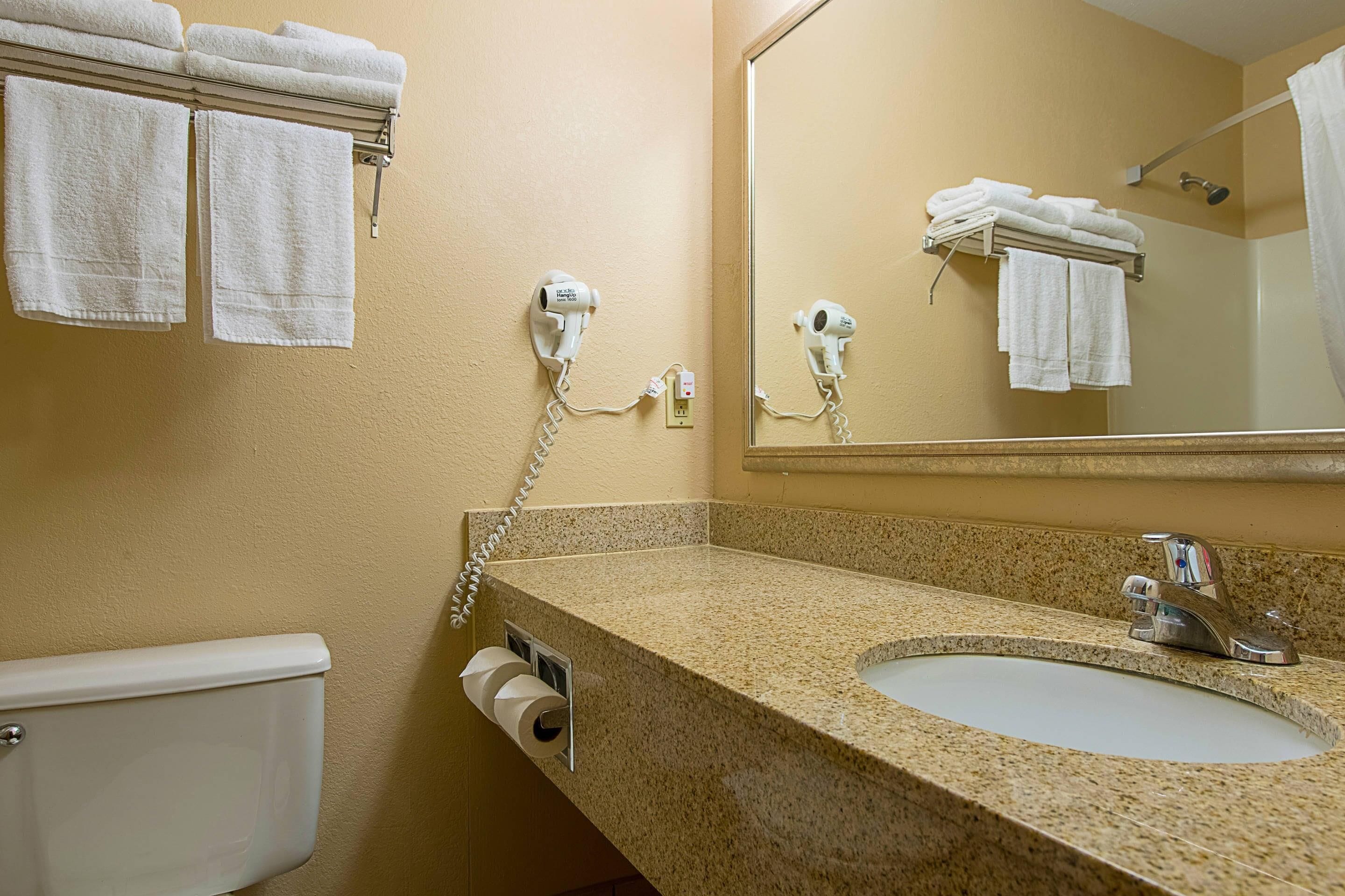Une salle de bain équipée d’un lavabo, de toilettes, d’un porte-serviettes et de deux sèche-cheveux fixés au mur.