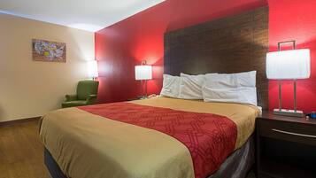A hotel room with a large bed, two bedside lamps, a green chair, and a wooden headboard.
