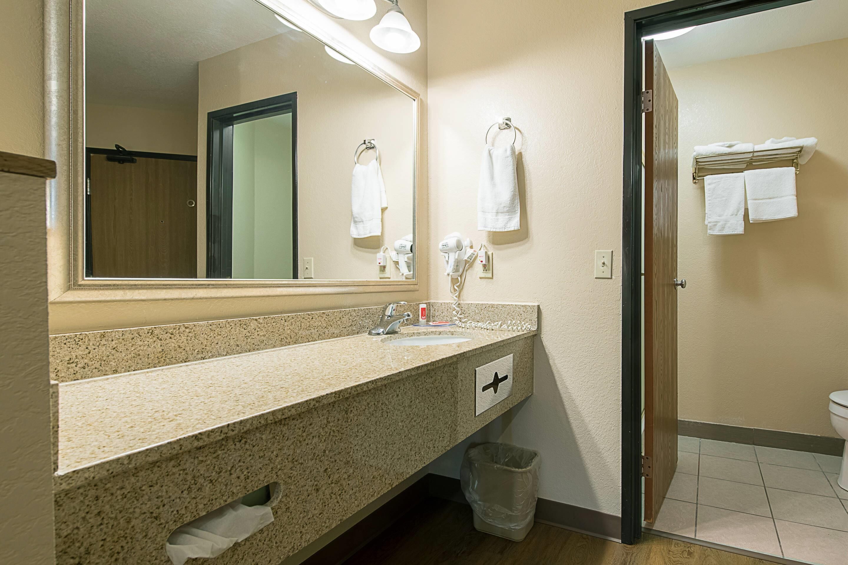 Baño con encimera de granito, espejo, toallero, secador de pelo y cubo de basura.