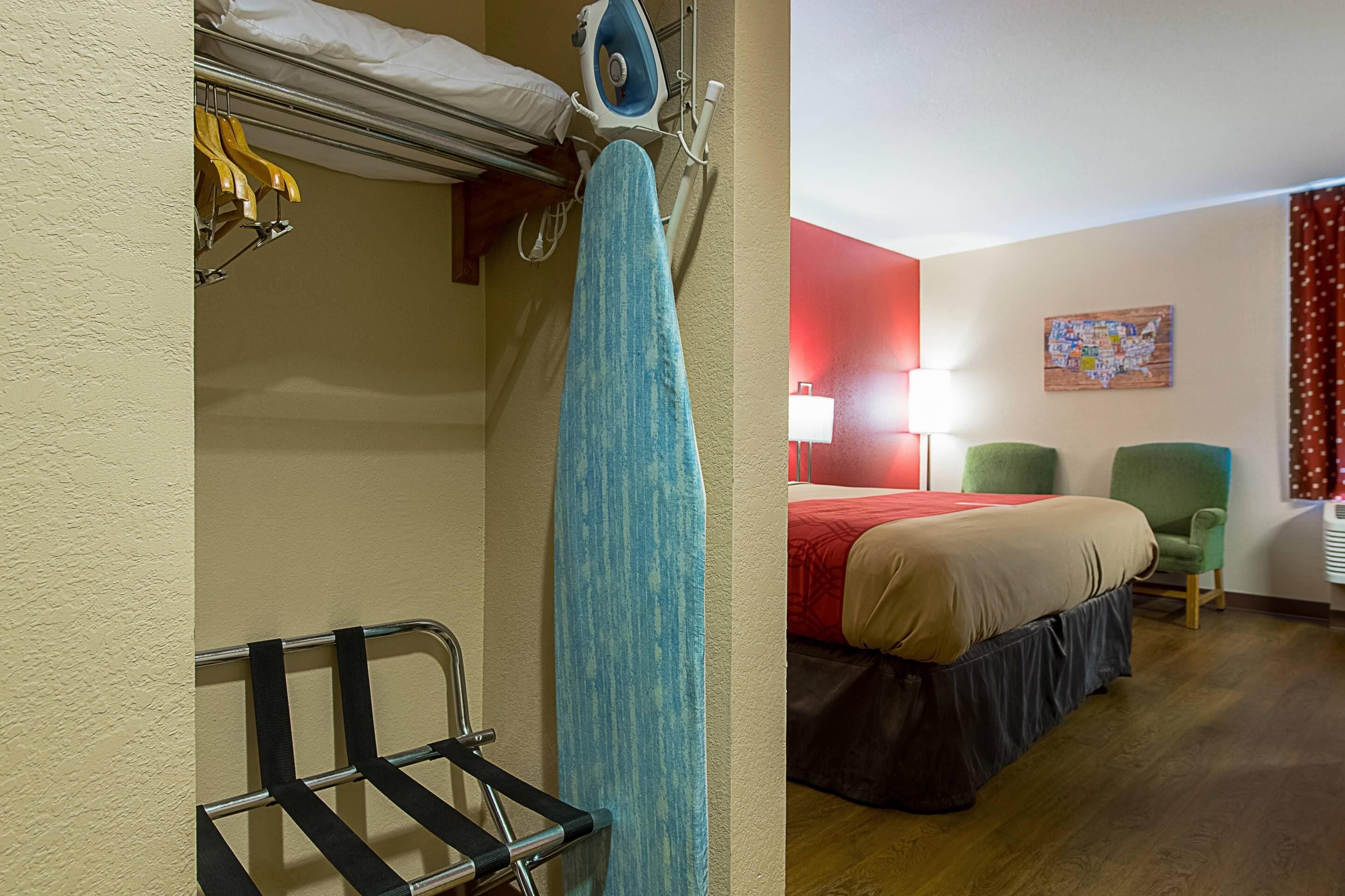 A hotel room with a bed, a chair, a hanging towel, and a wall-mounted ironing board.