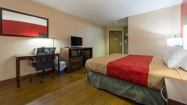 Quarto de hotel com cama, escrivaninha, cadeira, televisão e micro-ondas.
