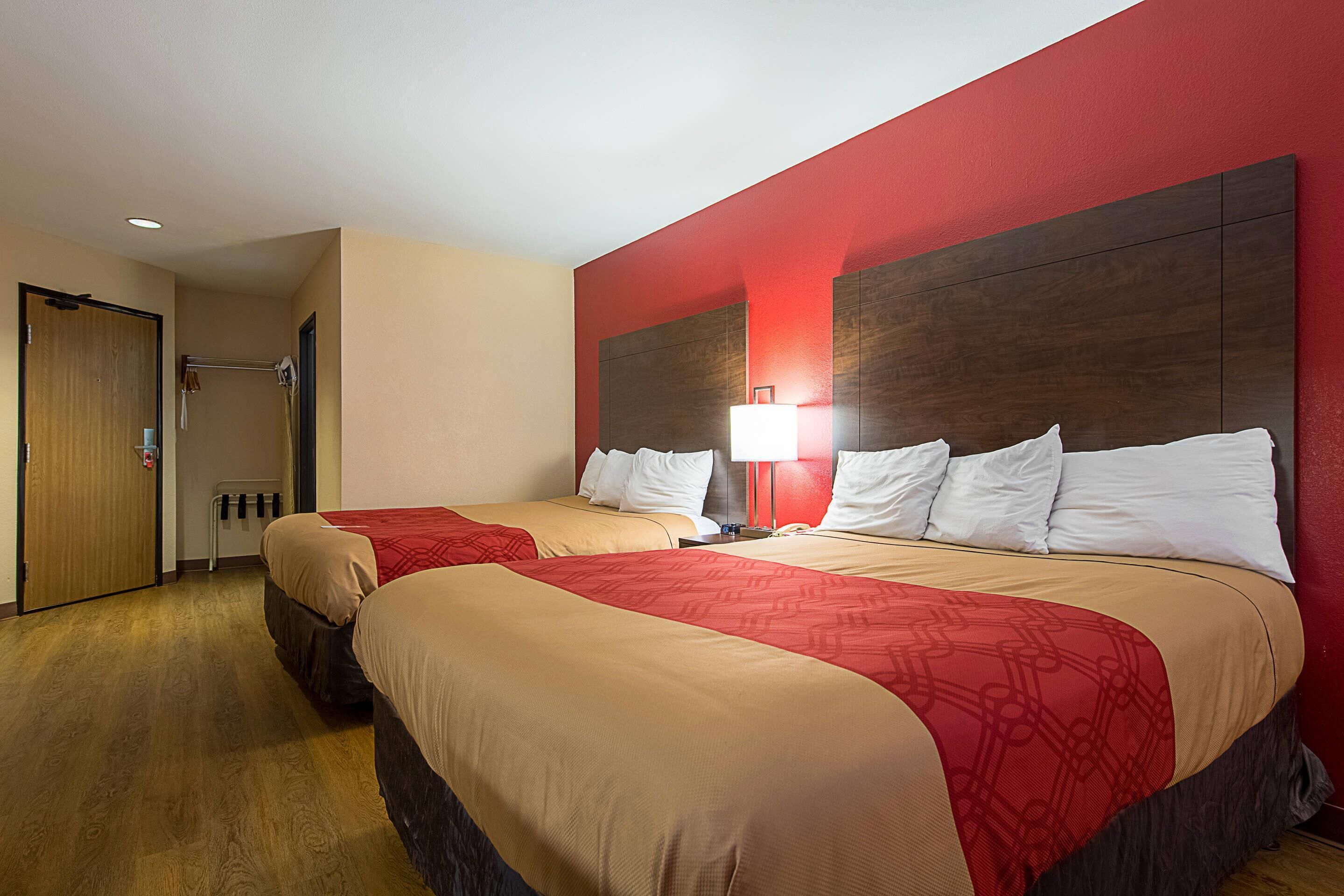 A hotel room with two beds, a red accent wall, and a wooden floor.