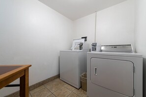 A laundry room with two washing machines, a dryer, and a small trash bin. - Econo Lodge Buckley Bonney Lake (Buckley)