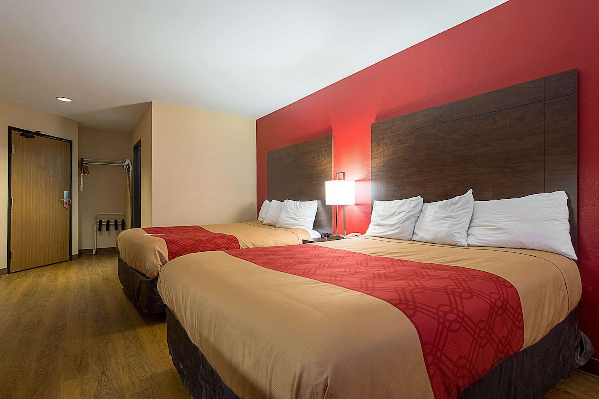 Une chambre d’hôtel avec deux lits, un mur d’accent rouge et un plancher en bois.