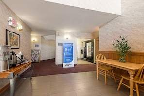 A hotel lobby with a coffee station, a reception desk, a dining area with a table and chairs, and a wall with a sign. - Econo Lodge Buckley Bonney Lake (Buckley)