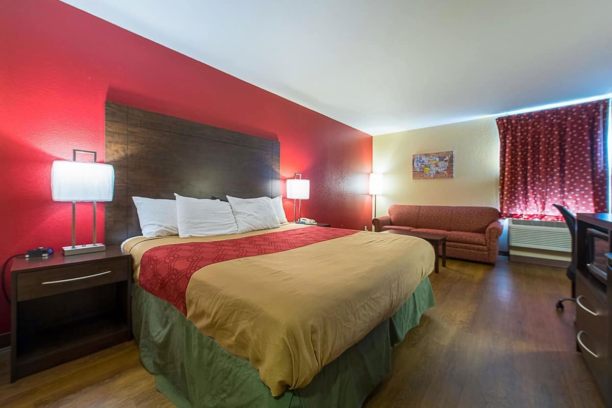 Une chambre d’hôtel avec un grand lit, deux lampes de chevet, un mur rouge, un canapé et un bureau avec une chaise.