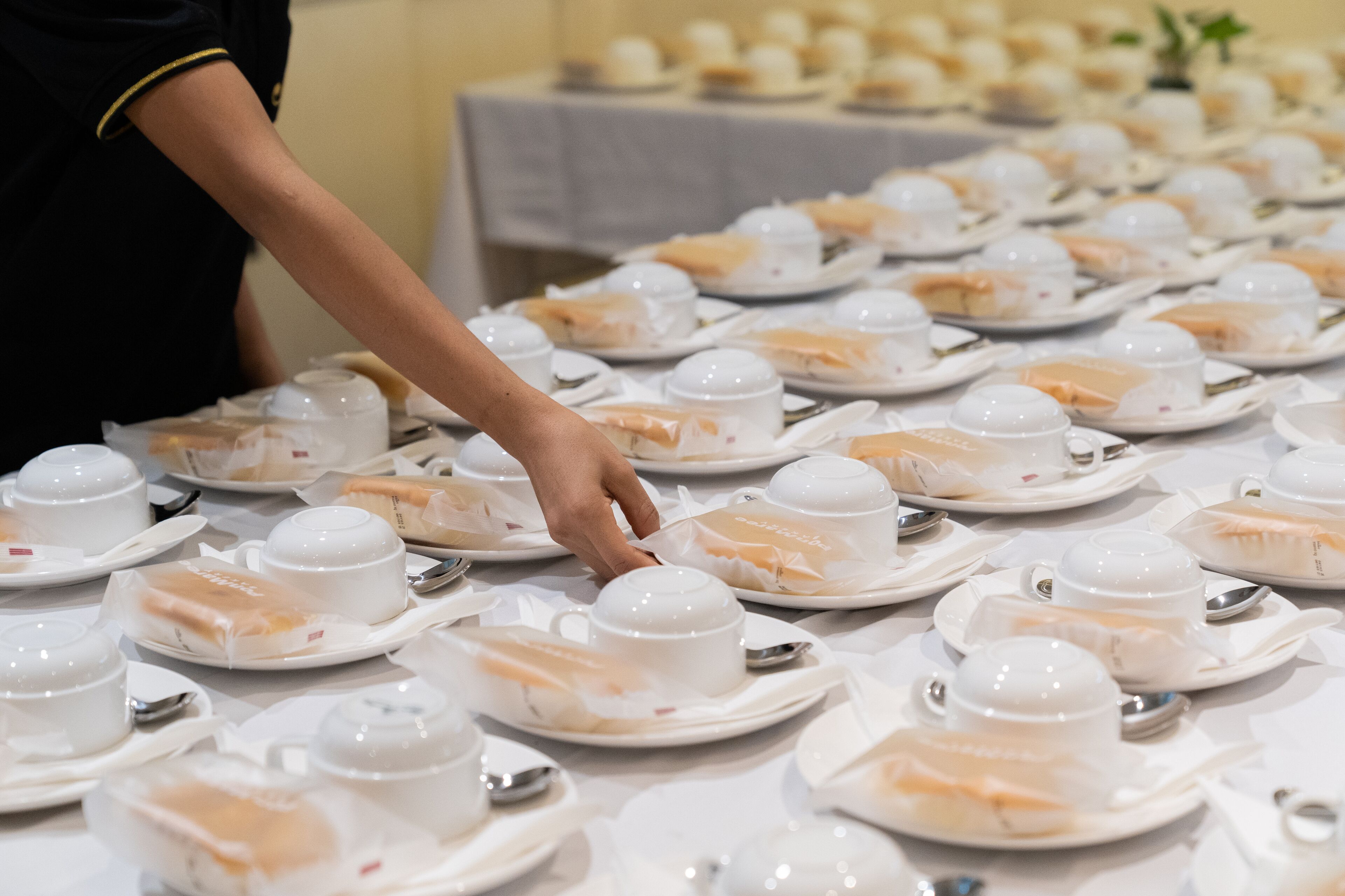 A table set with multiple white teacups and saucers, arranged neatly in rows.