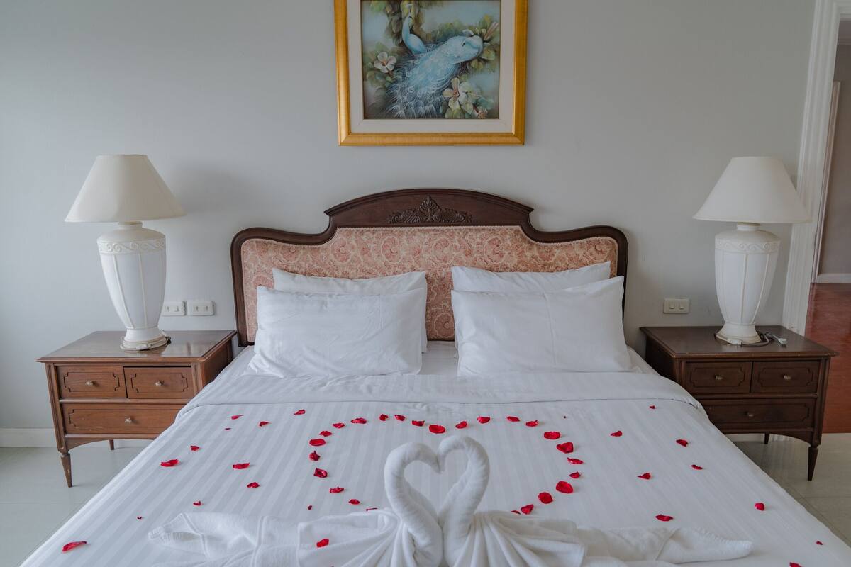 Una cama impecable con sábanas blancas y una decoración con forma de corazón hecha de pétalos de rosa.