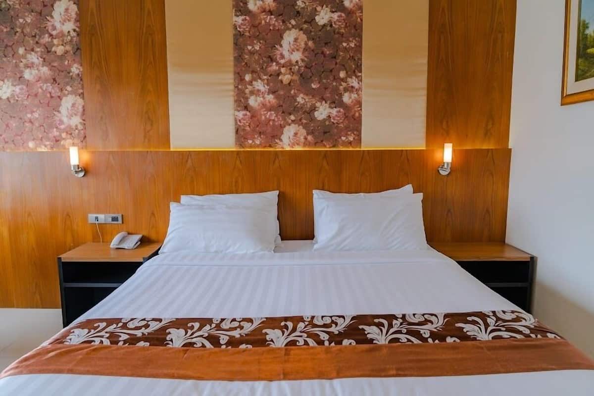 Habitación de hotel con cabecera de madera, dos mesitas de noche, un teléfono y un panel decorativo en la pared.