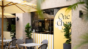 An outdoor seating area with striped umbrellas and chairs, a yellow wall with a sign, and potted plants. - Forum Park Hotel (Bangkok)