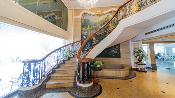 A grand staircase with ornate black railings and a chandelier, leading to an upper floor. - Forum Park Hotel (Bangkok)