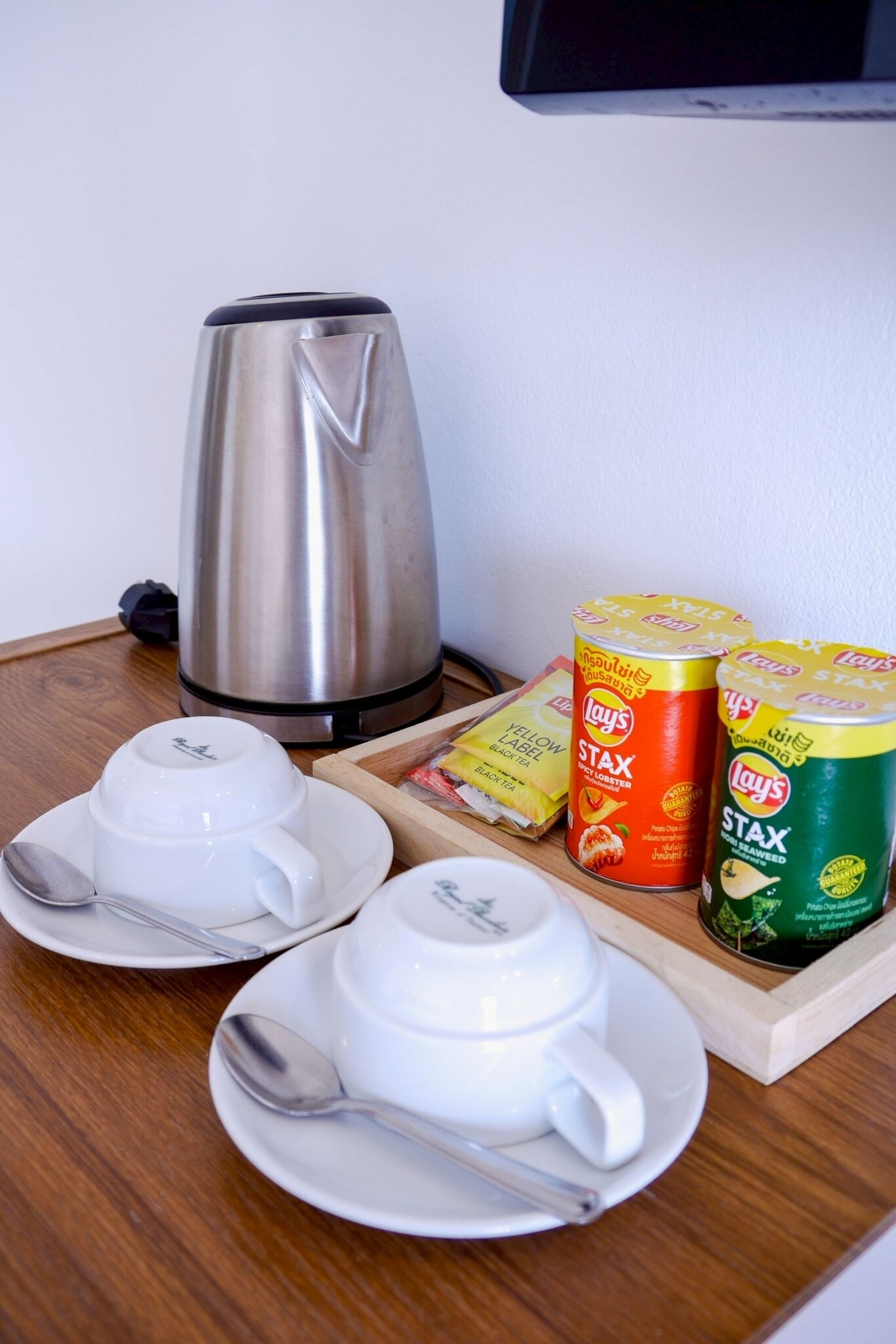 A table with a kettle, two white cups with saucers, and two cans of Stax instant coffee.