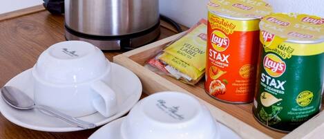 A table with a kettle, two white cups with saucers, and two cans of Stax instant coffee.