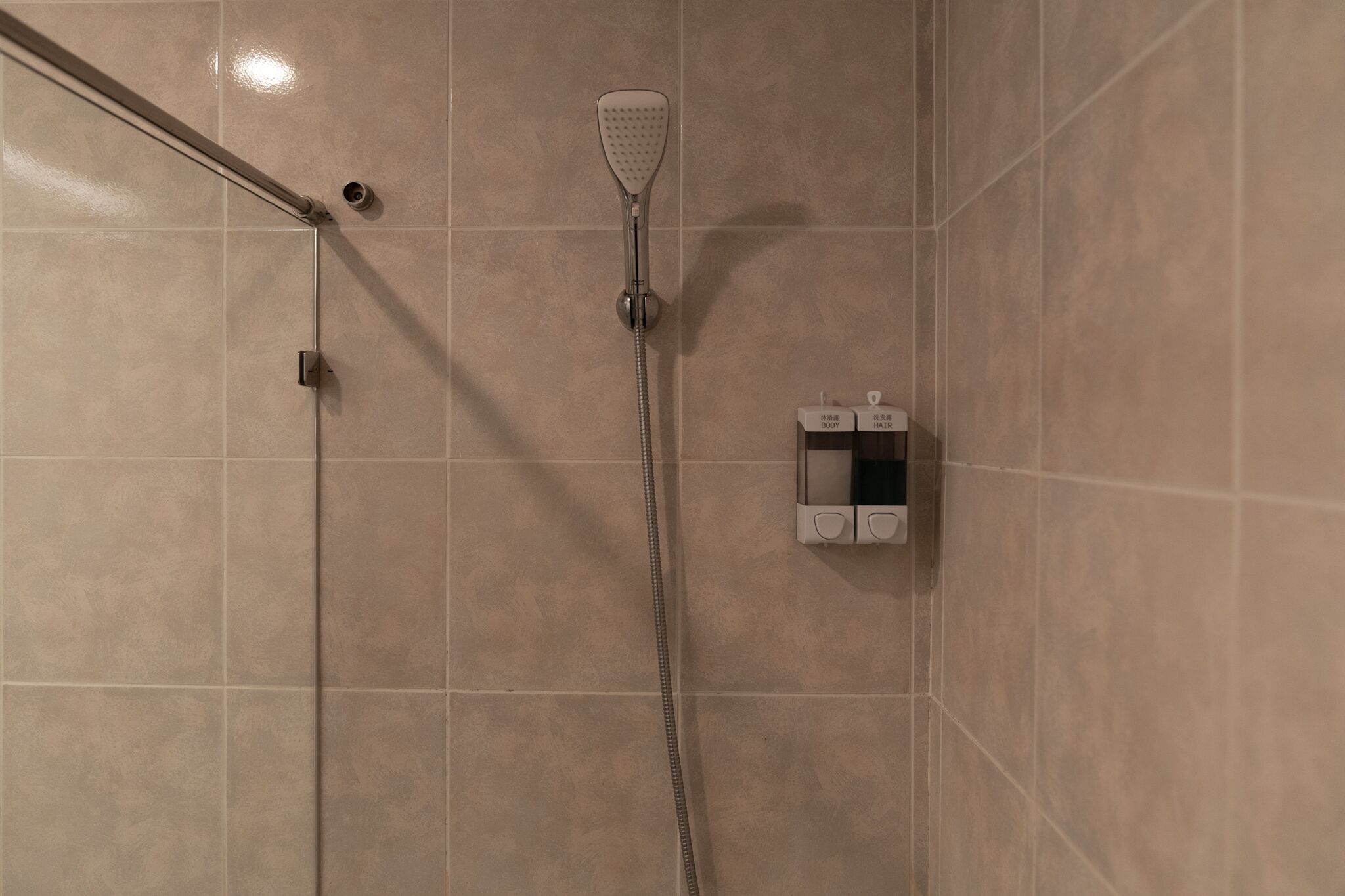 Una ducha con cabezal de ducha de mano y panel de control con botones etiquetados “CUERPO” y “CABELLO”.