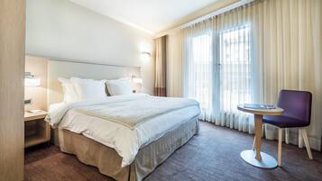 Una habitación de hotel con una cama grande, una mesita de noche, una silla y una ventana con cortinas.