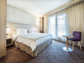 A hotel room with a large bed, a bedside table, a chair, and a window with curtains.