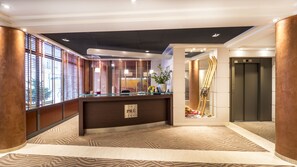 A reception area with a wooden reception desk, a potted plant, and a sign reading "LE PRÉ CARRÉ".