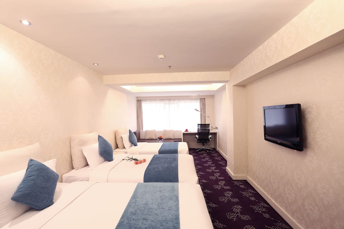A hotel room with two beds, a TV, a desk, and a window with curtains.