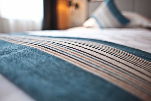 A close-up of a striped fabric, likely a bedspread or blanket, with a blurred background suggesting a room setting.
