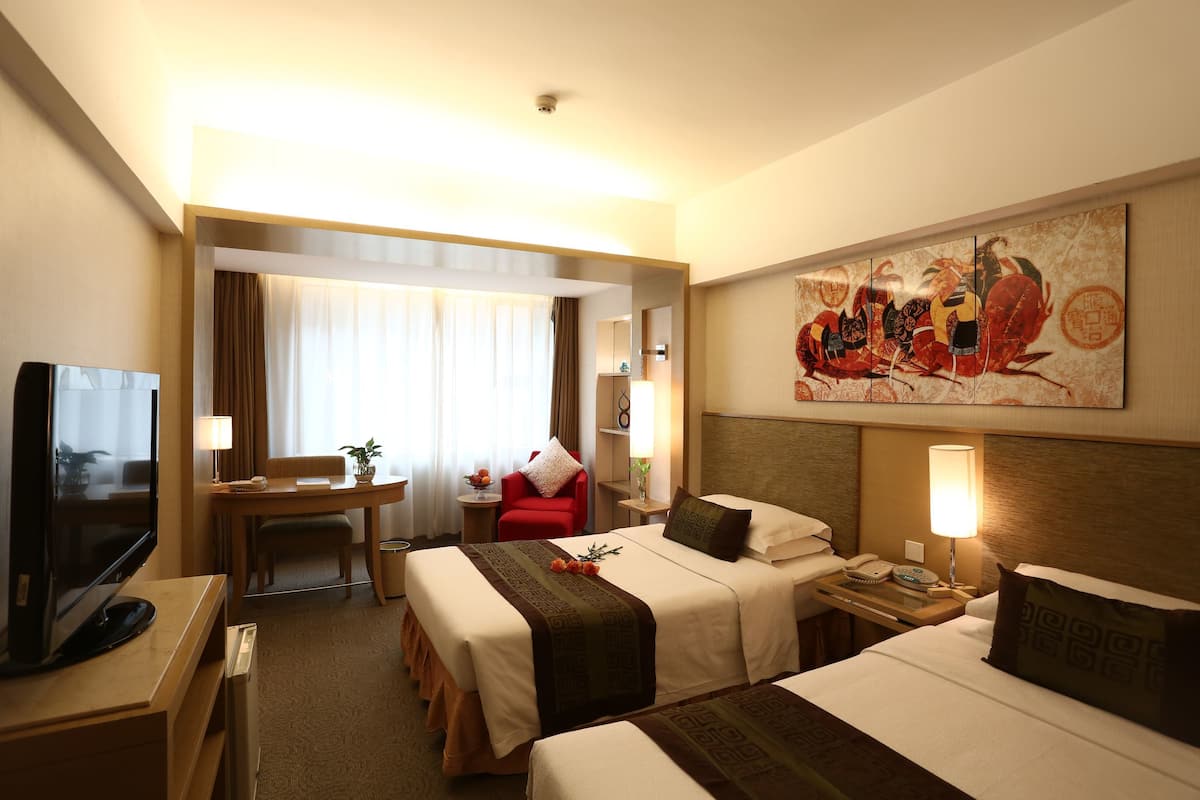 A hotel room with two beds, a desk, a television, and a painting on the wall.