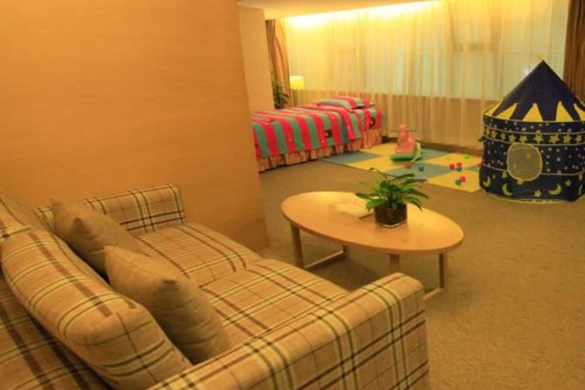 A cozy living room with a plaid sofa, a small round table with a plant, and a play area with a tent-like structure and toys.