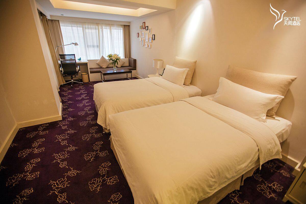 A hotel room with two beds, a desk, a chair, and a small table with a vase of flowers.