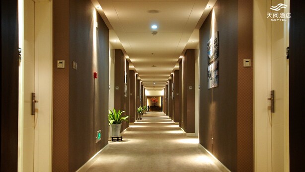 A hotel hallway with a carpeted floor, potted plants, and doors on both sides. - Skytel Xi'an (Xi'an)