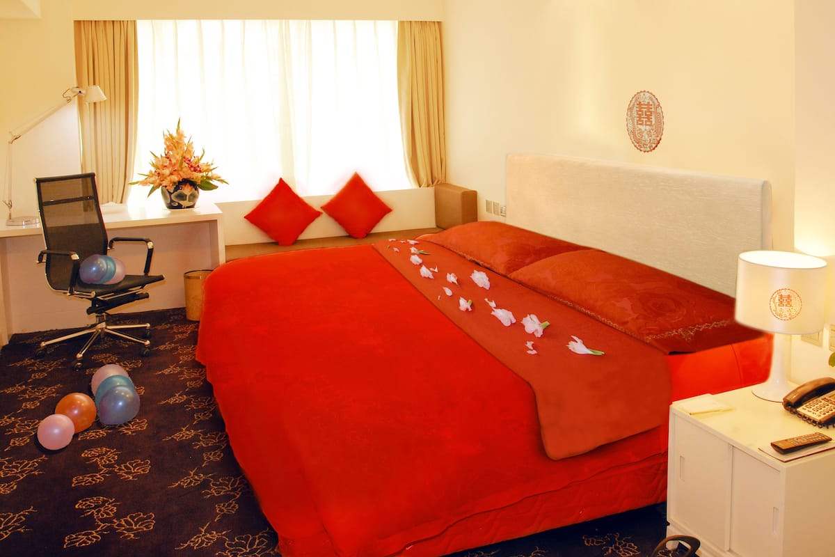 A hotel room with a large bed, a desk with a computer, a lamp, and a telephone.