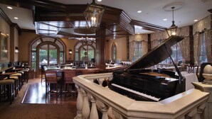 A grand piano in a spacious room with a high ceiling, large windows, and a bar area. - Bernards Inn (Bernardsville)