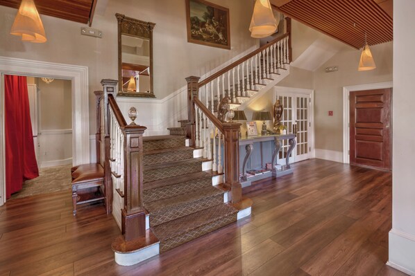 A grand staircase with wooden railings and a patterned carpet, leading to a landing with a glass coffee table and decorative items.