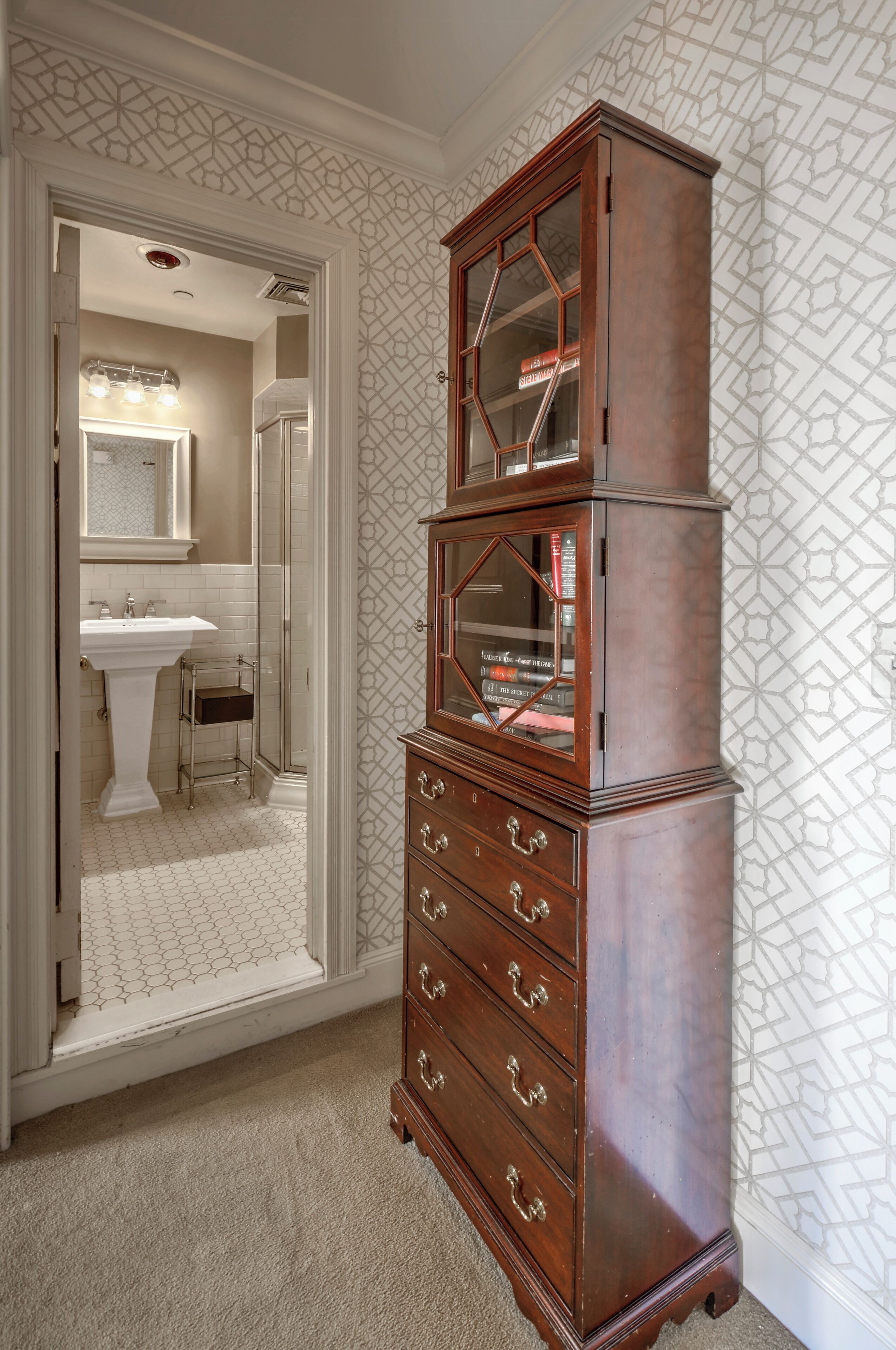 A room with a wooden cabinet with multiple drawers and a mirror, a white sink, and a patterned wall.