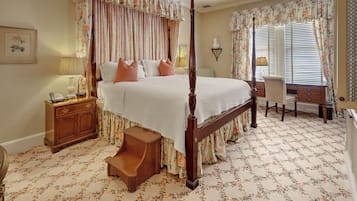 A four-poster bed with a wooden frame, a nightstand with a lamp, a chair, and a desk with a lamp.