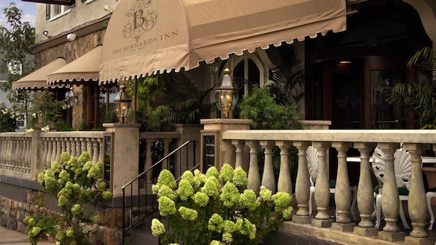A hotel facade with a classic architectural style, featuring a large marquee sign, a covered entrance, and a stone balustrade. - Bernards Inn (Bernardsville)
