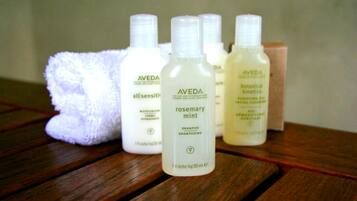 Superficie de madera con varios productos de cuidado de la piel Aveda, incluyendo una botella de champú romero y menta, junto con otros artículos.