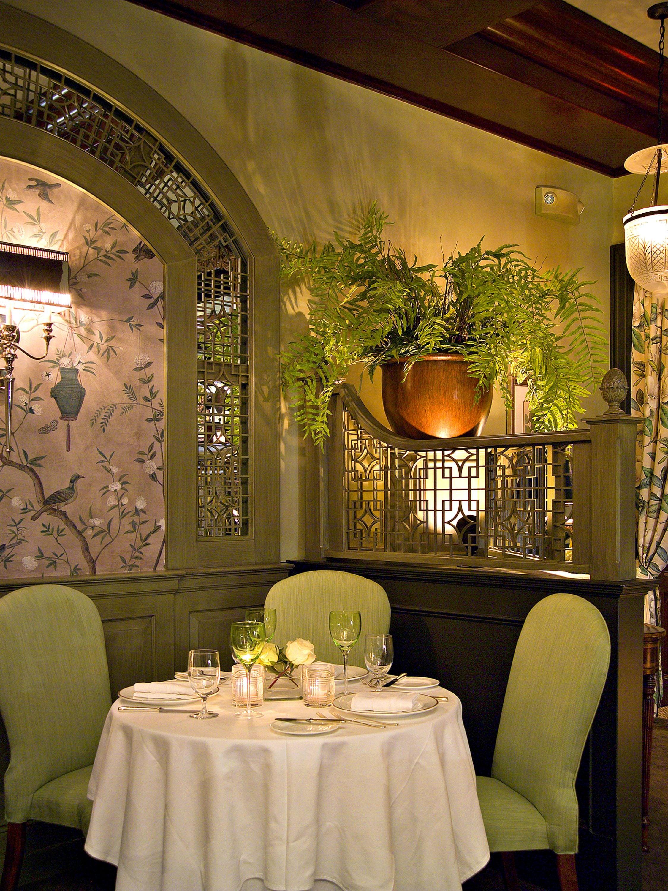 A dining area with a table set for two, a potted plant, and a decorative wall with a floral pattern.