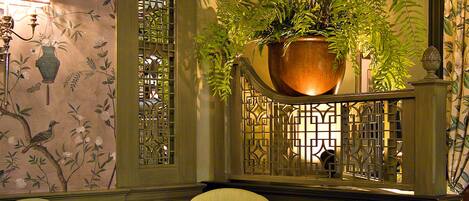 Un coin repas avec une table dressée pour deux personnes, une plante en pot et un mur décoratif orné d’un motif floral.