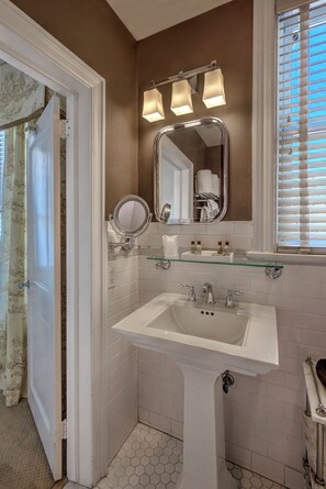 A bathroom with a white sink, a mirror, and a window with blinds.