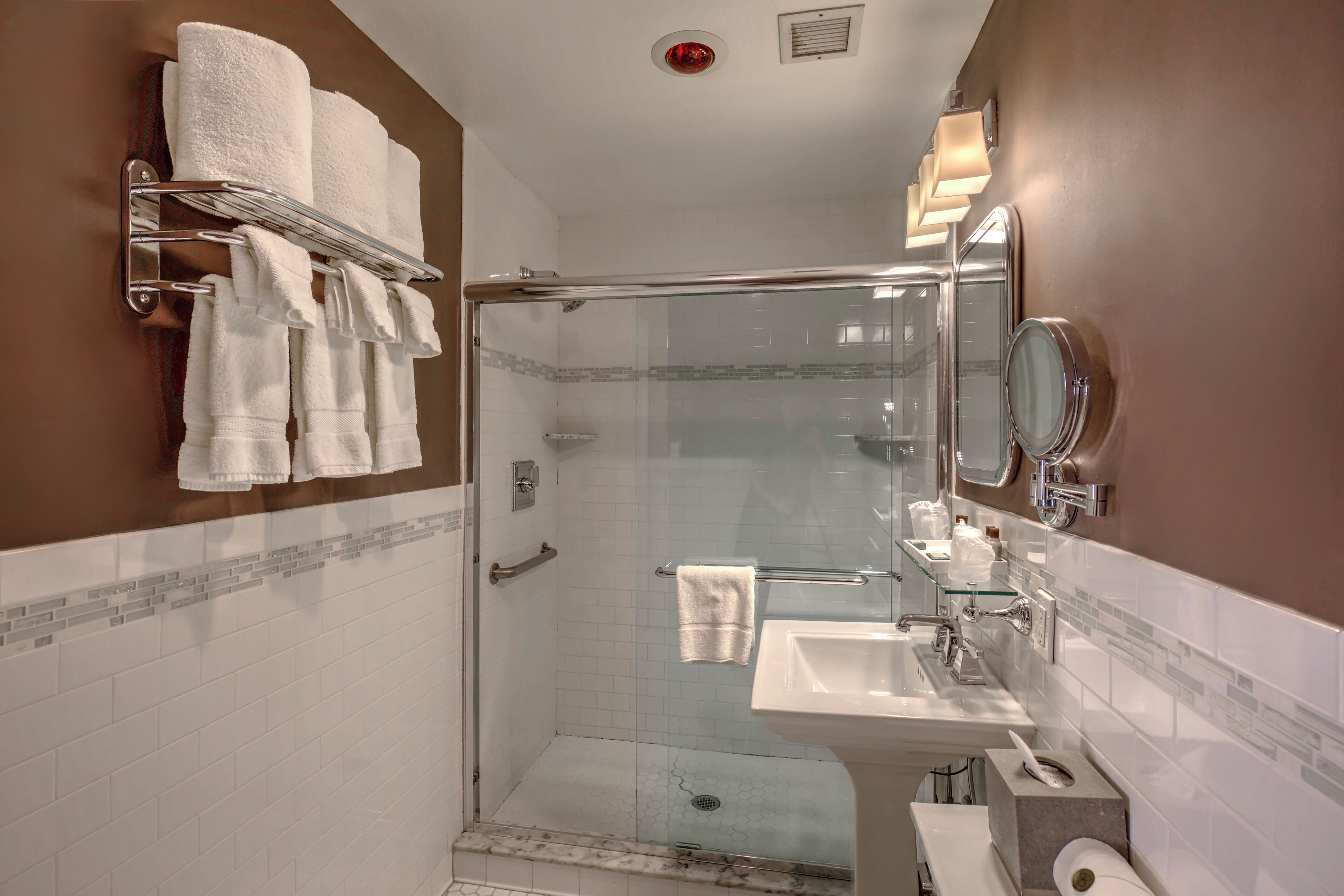 Un baño moderno con ducha de vidrio, tocador con espejo y toallero con varias toallas.
